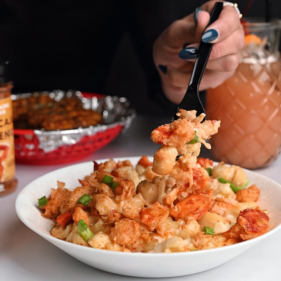 A person's hand with blue nails uses a fork to scoop up creamy lobster mac and cheese.