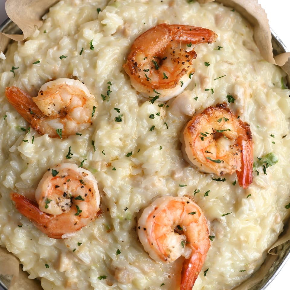 Creamy seafood risotto with five large, perfectly cooked shrimp and fresh parsley in a metal pan.