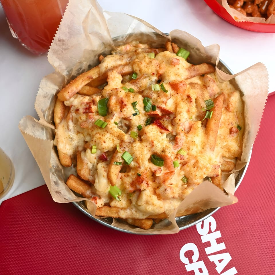 Shaking Crab's Cajun fries topped with creamy sauce, shrimp, and green onions in a metal bowl.