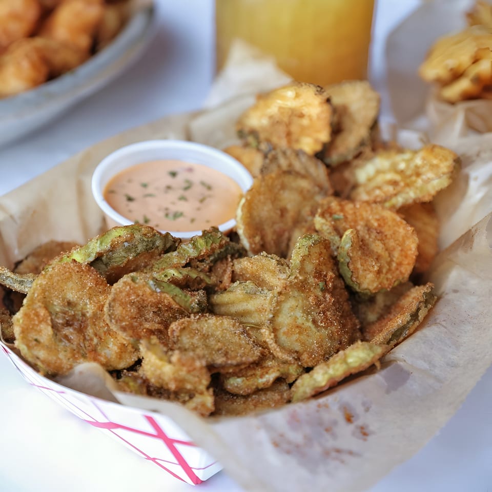 A basket of crispy fried pickles with a side of creamy dipping sauce, from Shaking Crab.